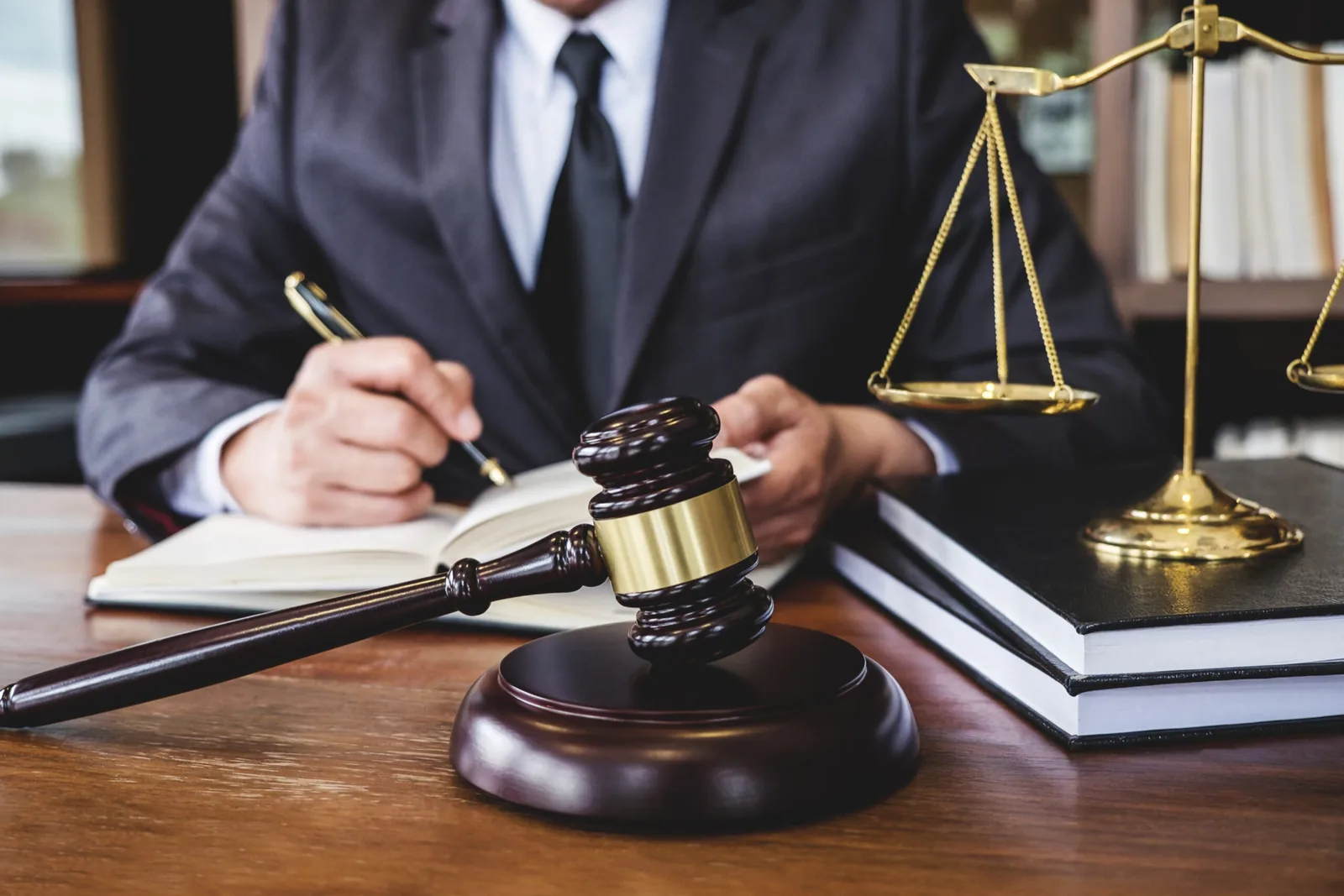 Legal professional writing beside a gavel and the scales of justice